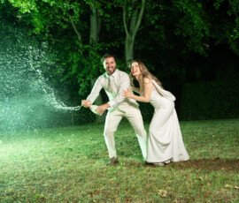Brautpaar öffnet eine Champagnerflasche im Grünen, umgeben von Blitzlicht bei einer emotionalen Hochzeitsfeier. Exklusive Hochzeitsfotografie und Hochzeitsvideografie in Stuttgart von Majestic Wedding.